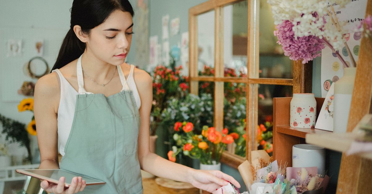A florist holding a tablet in a flower shop next to wrapped bouquets.