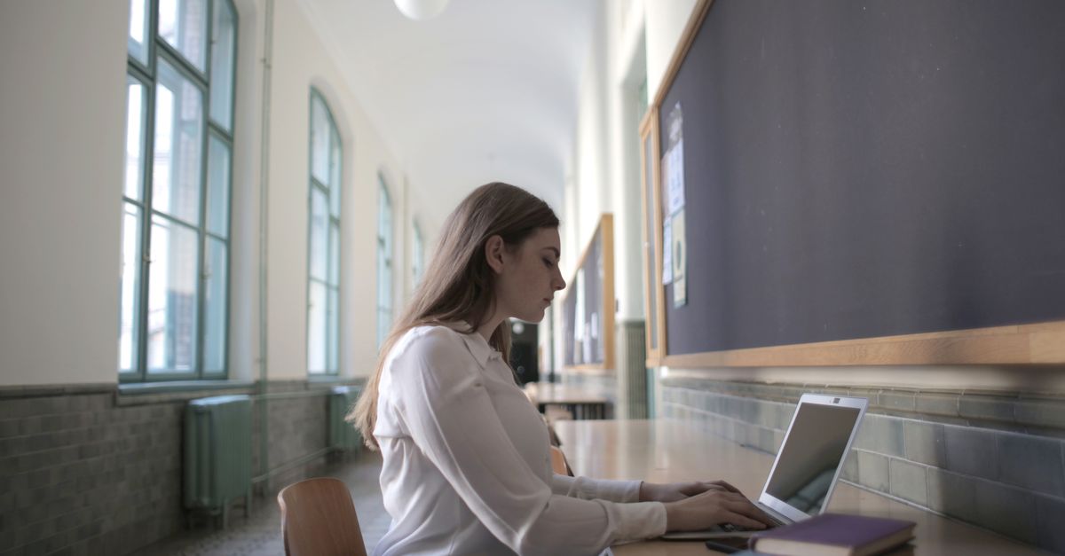 A focused young woman typing on a laptop while sitting at a table with books.