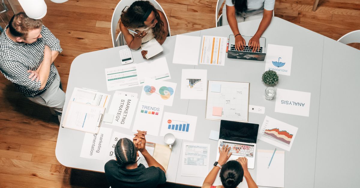 A diverse group of colleagues in an office discussing marketing strategies around charts and laptops.