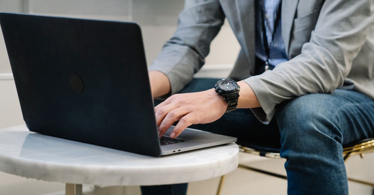 A man typing on a laptop keyboard at a desk in a modern office.