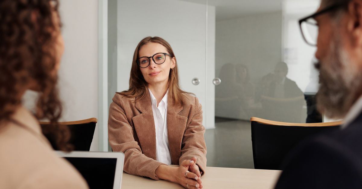 A young woman seated at a table during a job interview in a modern office.
