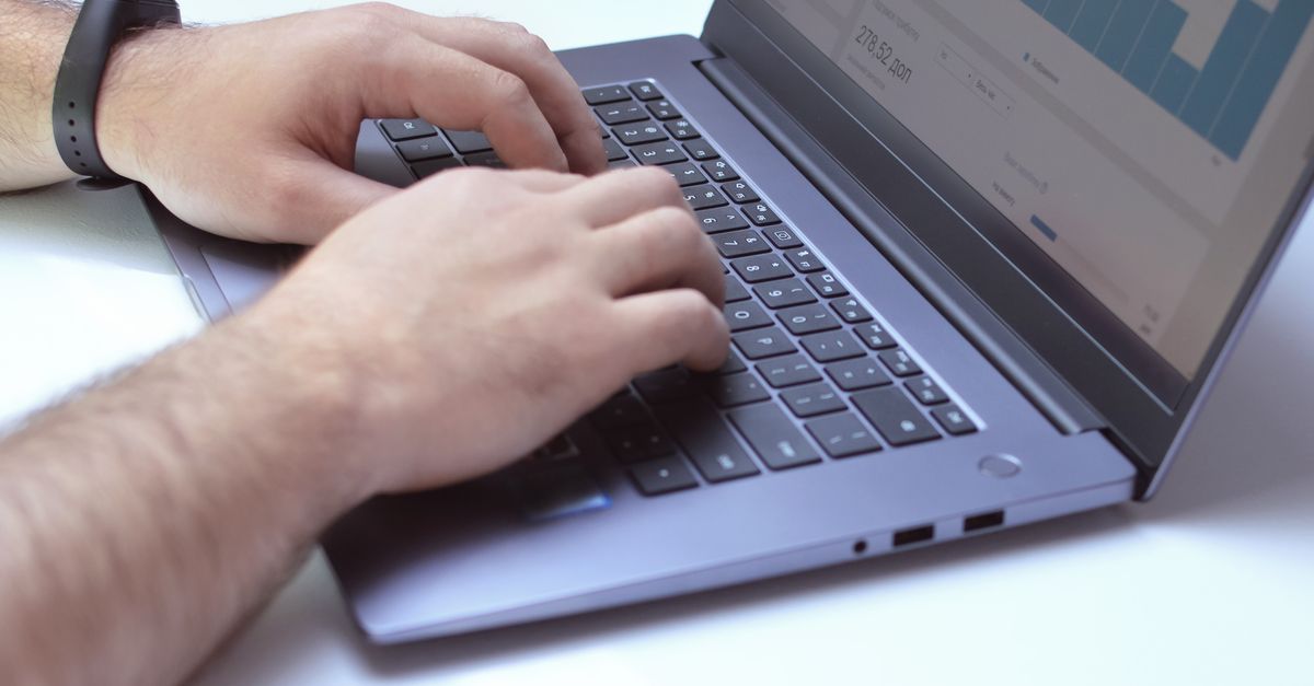 An analyst typing on a laptop while working with data and analytical graphs in an office.