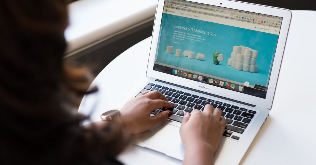 A businesswoman seated at a table, working on a laptop with a webpage open on the screen.